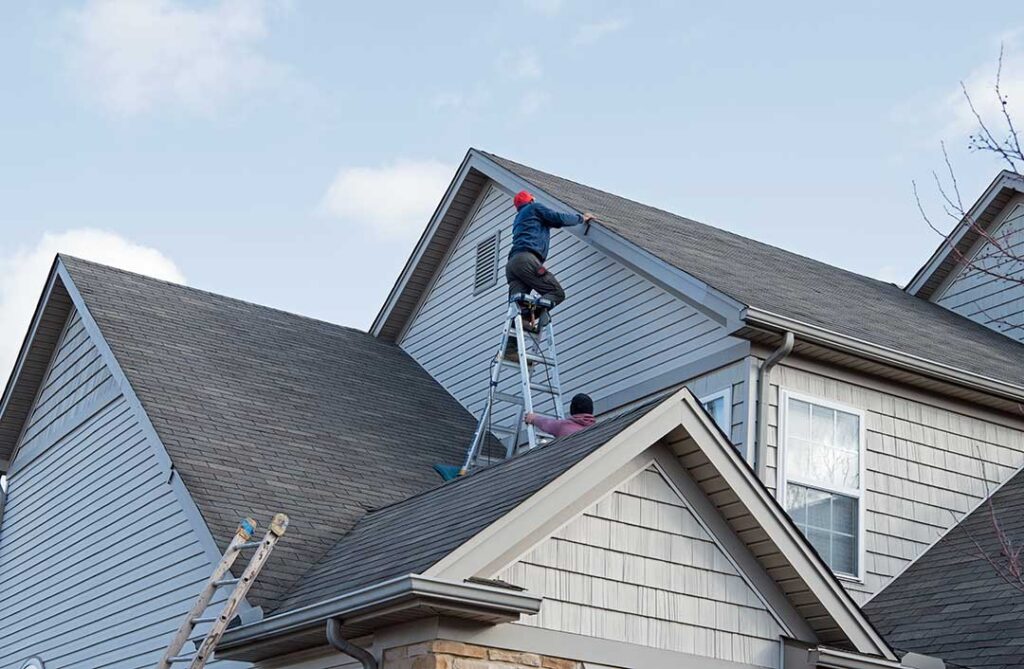 Snow-covered residential roof with clear gutters, roof flashing, and winter trees after a storm.